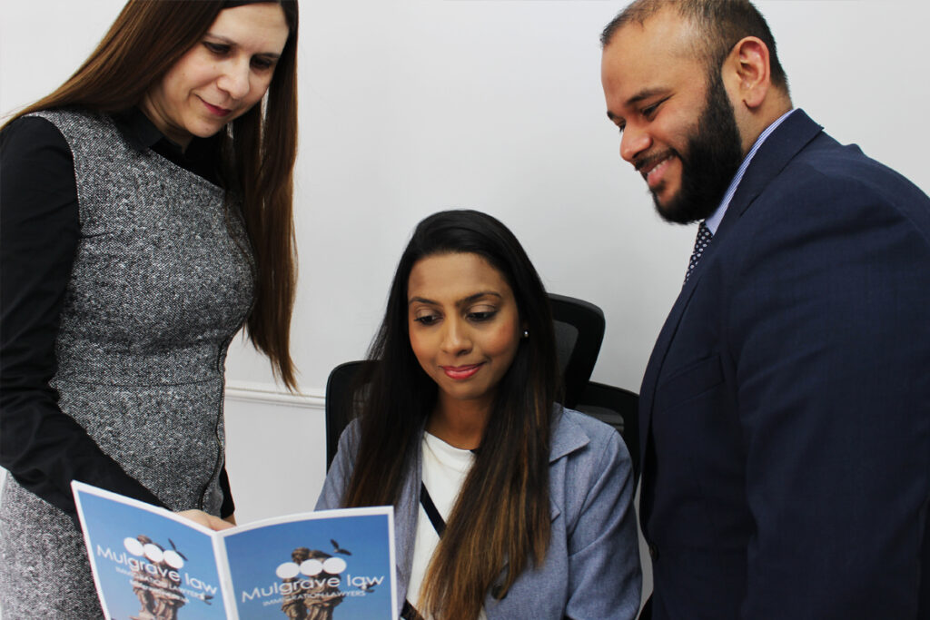 Three individuals in a professional consultation at the Mulgrave Law office, leading immigration lawyers in London, with one person holding a brochure.